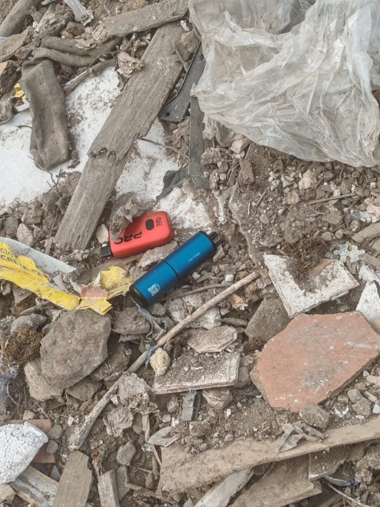 Photo showing a red and blue vape mixed in with rubbish and hardcore